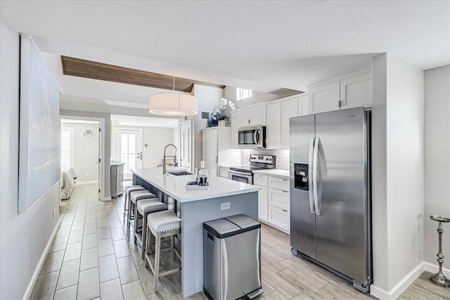 kitchen featuring stainless steel appliances, sink, a center island with sink, white cabinetry, and hanging light fixtures