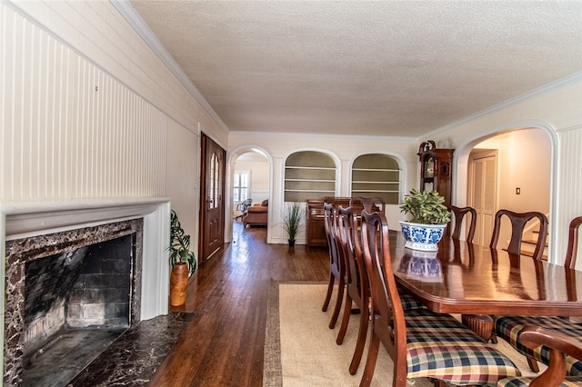 dining space with dark wood-type flooring, a textured ceiling, a premium fireplace, and crown molding