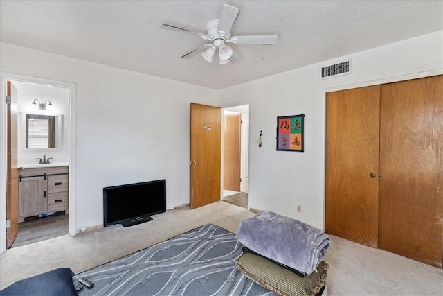 bedroom featuring light carpet, ceiling fan, ensuite bath, a closet, and sink