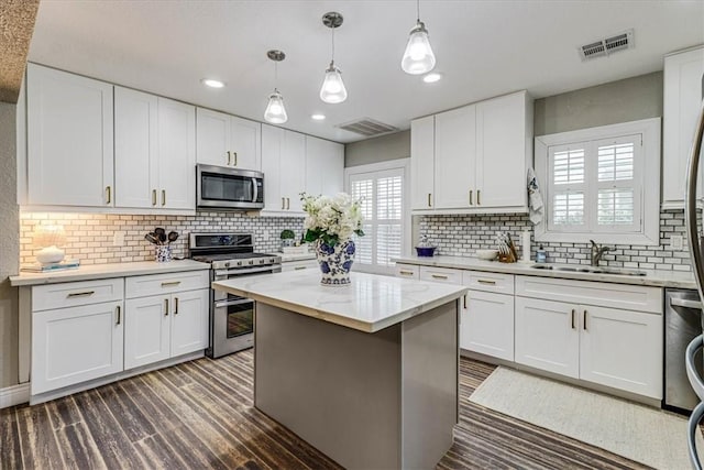 kitchen with sink, hanging light fixtures, appliances with stainless steel finishes, a kitchen island, and white cabinets