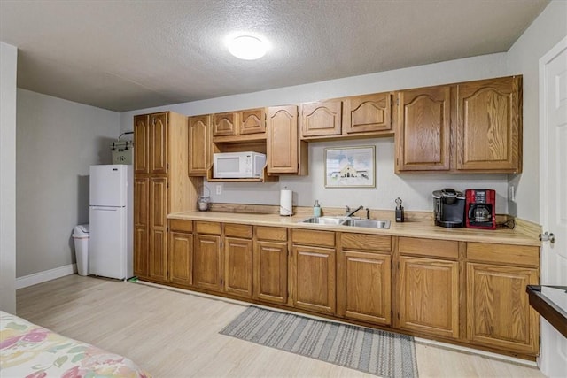 kitchen with sink, white appliances, light hardwood / wood-style flooring, and a textured ceiling