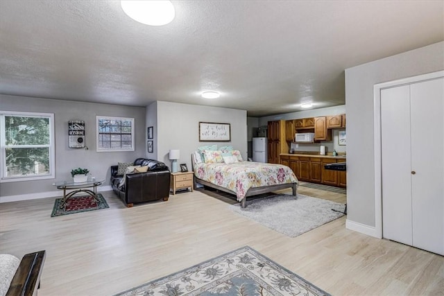 bedroom featuring light hardwood / wood-style floors, a textured ceiling, and white fridge