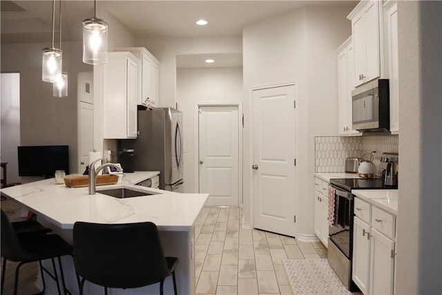 kitchen featuring a kitchen bar, appliances with stainless steel finishes, sink, pendant lighting, and white cabinets