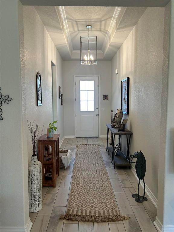 doorway with a chandelier, ornamental molding, and a tray ceiling