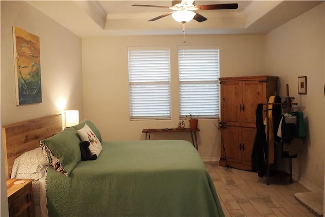 bedroom with ceiling fan, a raised ceiling, ornamental molding, and light hardwood / wood-style flooring