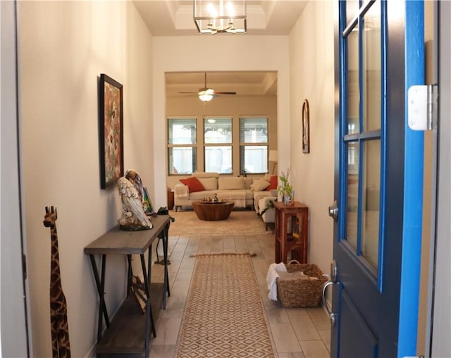 tiled foyer featuring a tray ceiling and ceiling fan with notable chandelier