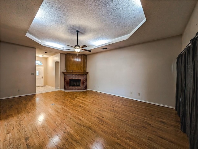 14929 Red River Dr, Corpus Christi, TX 78410 - unfurnished living room with a textured ceiling, ceiling fan, wood finished floors, a fireplace, and a tray ceiling