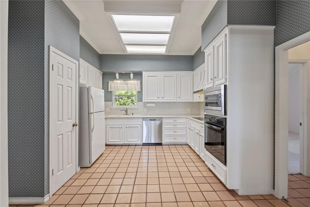 kitchen featuring stainless steel appliances, a sink, wallpapered walls, light countertops, and white cabinets