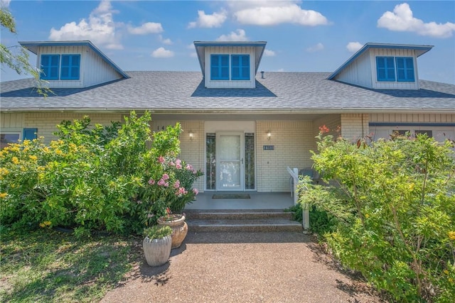 doorway to property with brick siding, roof with shingles, and a porch