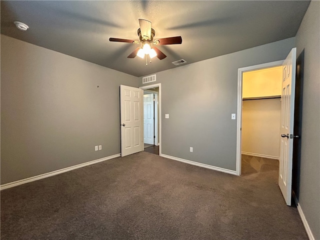 unfurnished bedroom with dark colored carpet, a spacious closet, ceiling fan, and a closet