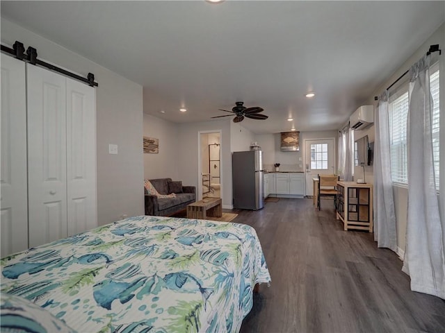 bedroom featuring stainless steel refrigerator, a wall mounted air conditioner, a barn door, and dark hardwood / wood-style flooring