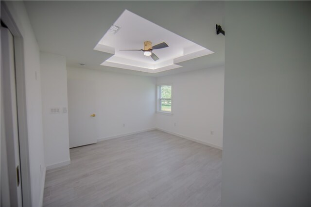 unfurnished room featuring ceiling fan, a raised ceiling, and light hardwood / wood-style flooring