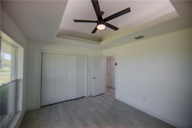 unfurnished bedroom with ceiling fan, a raised ceiling, light hardwood / wood-style flooring, and a closet