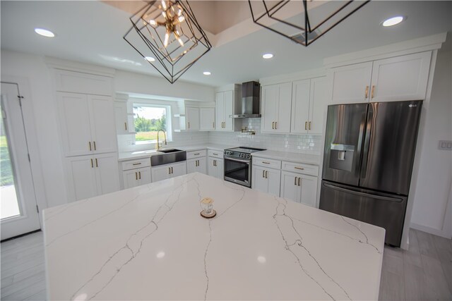 kitchen with wall chimney range hood, appliances with stainless steel finishes, light stone counters, and hanging light fixtures