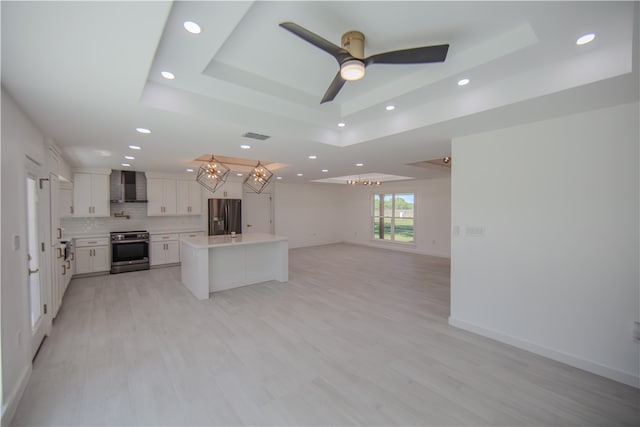 kitchen featuring stainless steel appliances, a kitchen island, white cabinetry, a raised ceiling, and wall chimney exhaust hood