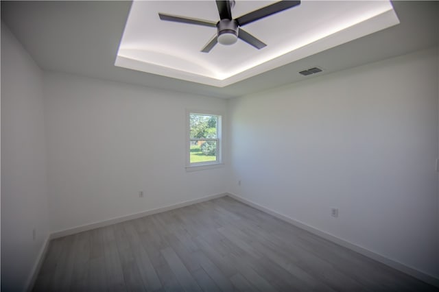 empty room featuring hardwood / wood-style flooring, ceiling fan, and a tray ceiling