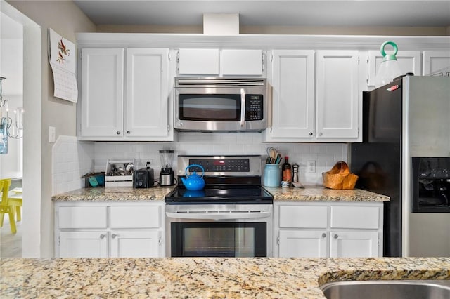 kitchen with light stone countertops, white cabinetry, backsplash, and appliances with stainless steel finishes