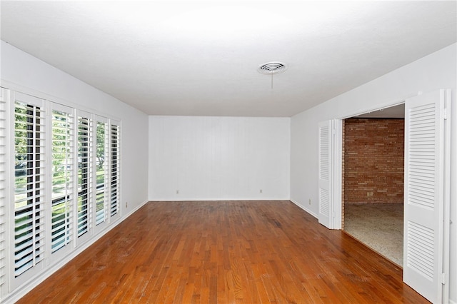 unfurnished room featuring dark hardwood / wood-style flooring and brick wall