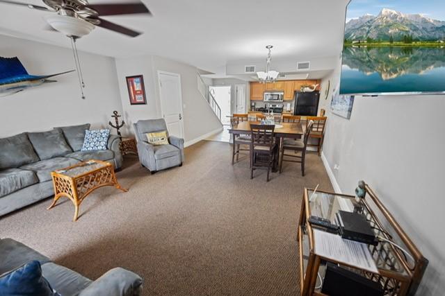 living room featuring ceiling fan with notable chandelier, plenty of natural light, and light carpet