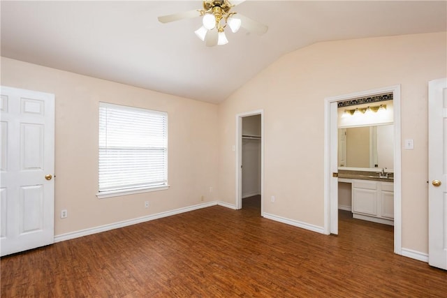 unfurnished bedroom featuring a walk in closet, a sink, dark wood finished floors, baseboards, and vaulted ceiling