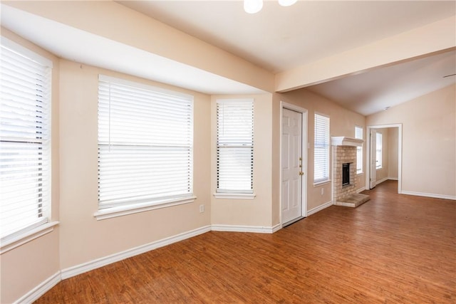 unfurnished living room with lofted ceiling, wood finished floors, baseboards, and a fireplace with raised hearth