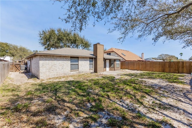 rear view of house with brick siding, a chimney, a yard, a fenced backyard, and a patio area