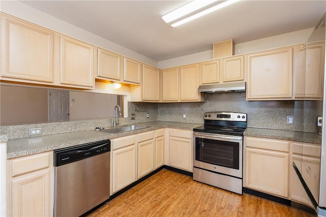 kitchen featuring light wood finished floors, light brown cabinetry, a sink, under cabinet range hood, and appliances with stainless steel finishes