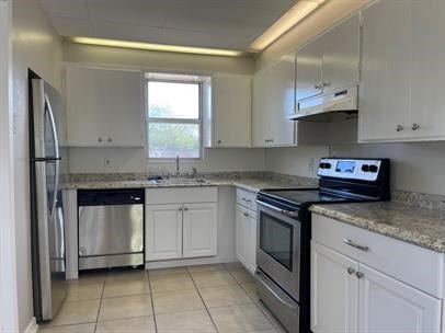 kitchen with light tile patterned floors, under cabinet range hood, appliances with stainless steel finishes, a sink, and white cabinetry