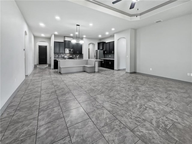 kitchen featuring a center island with sink, ceiling fan, stainless steel appliances, and tasteful backsplash