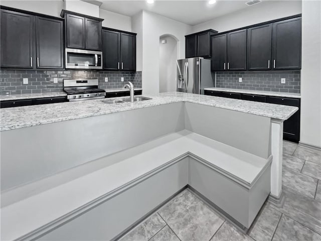 kitchen featuring light stone countertops, appliances with stainless steel finishes, backsplash, and sink