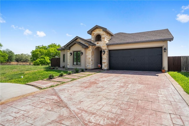 view of front facade with stone siding, roof with shingles, fence, an attached garage, and decorative driveway