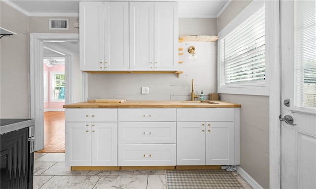 kitchen featuring butcher block countertops, sink, ornamental molding, and white cabinets