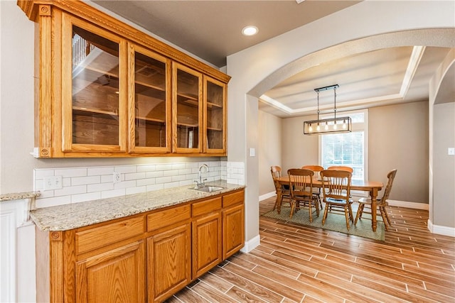 7601 Dijon Lake Dr, Corpus Christi, TX 78413 - kitchen featuring arched walkways, a tray ceiling, light wood finished floors, tasteful backsplash, and light stone counters