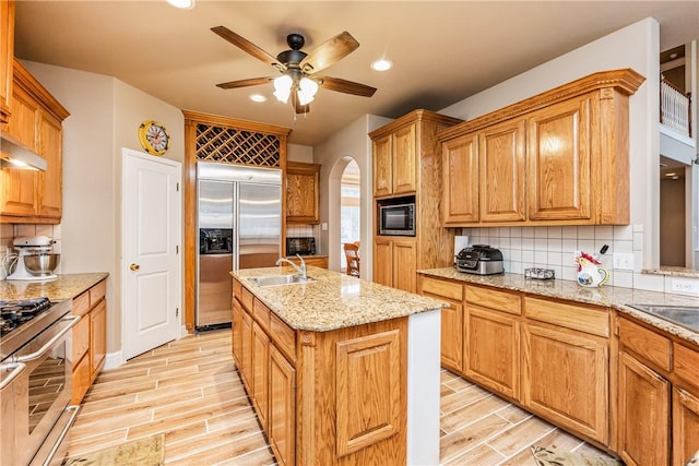 7601 Dijon Lake Dr, Corpus Christi, TX 78413 - kitchen featuring arched walkways, built in appliances, wood finish floors, a ceiling fan, and an island with sink