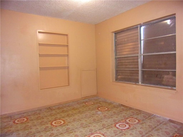 spare room with built in shelves and a textured ceiling