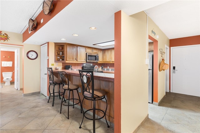 kitchen with range, stainless steel microwave, a breakfast bar, freestanding refrigerator, and open shelves