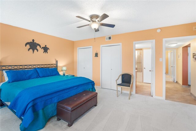 bedroom with a ceiling fan, two closets, and light colored carpet