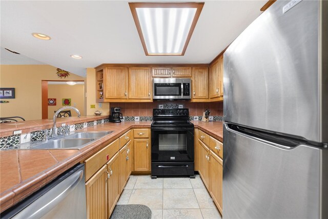 kitchen featuring tile countertops, decorative backsplash, appliances with stainless steel finishes, light tile patterned flooring, and a sink