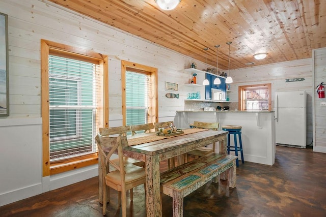 dining area featuring concrete floors, baseboards, wooden walls, and wood ceiling