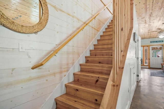 staircase featuring wooden ceiling, concrete floors, and wood walls