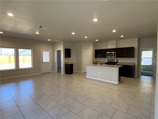 kitchen with a center island with sink, light stone counters, sink, light tile patterned floors, and appliances with stainless steel finishes