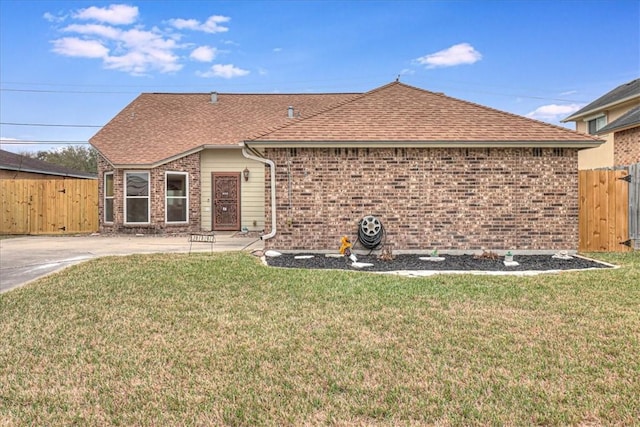 back of property with a yard, brick siding, roof with shingles, and a gate