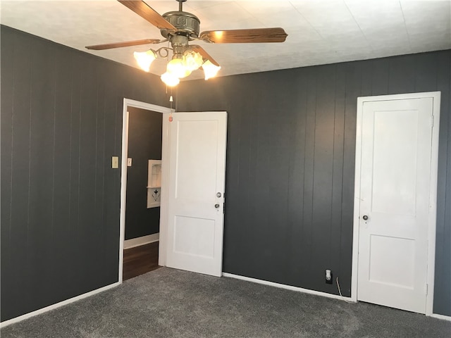 unfurnished bedroom featuring ceiling fan, wooden walls, and dark carpet