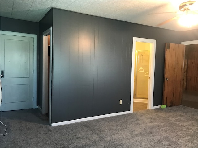 unfurnished bedroom with connected bathroom, wood walls, ceiling fan, and dark carpet