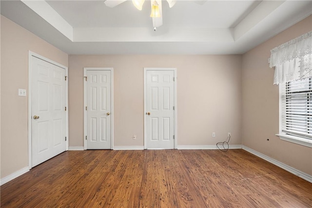 unfurnished bedroom featuring a tray ceiling, wood finished floors, and baseboards