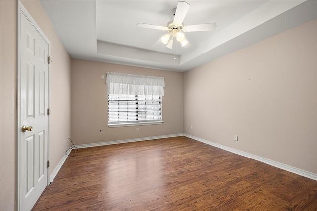 spare room featuring a raised ceiling, wood finished floors, a ceiling fan, and baseboards