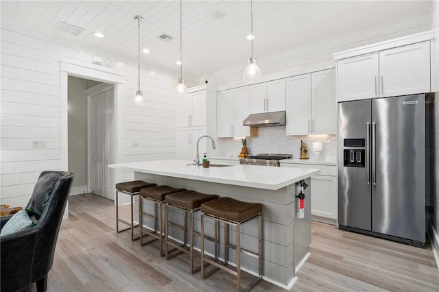 kitchen featuring high end fridge, sink, decorative light fixtures, an island with sink, and white cabinets