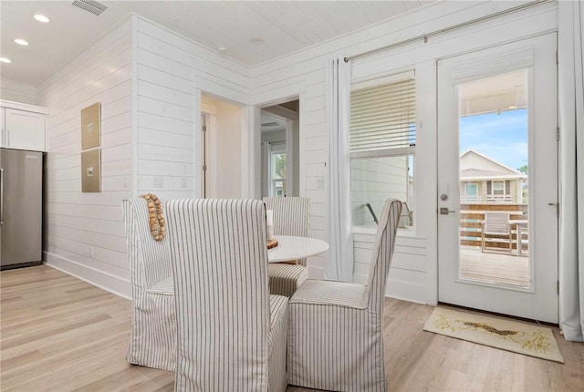 dining room with a wealth of natural light, light hardwood / wood-style floors, and wood walls