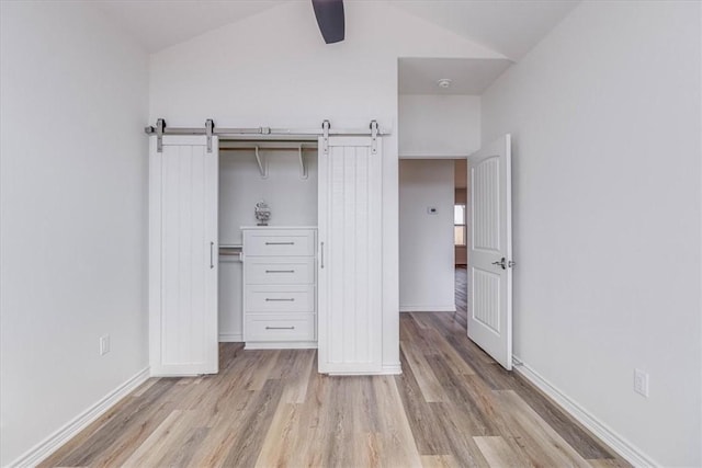 unfurnished bedroom with lofted ceiling, light hardwood / wood-style flooring, ceiling fan, a barn door, and a closet