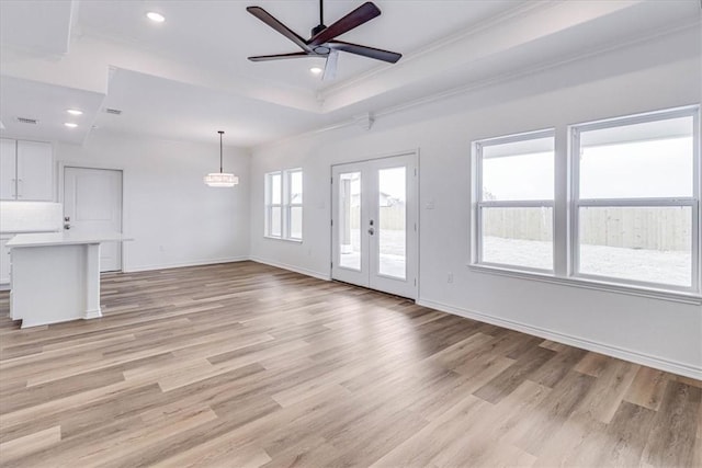 unfurnished living room with crown molding, ceiling fan, a raised ceiling, french doors, and light wood-type flooring